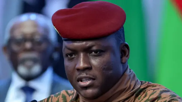 Portrait d'Ibrahim Traoré en tenue militaire beige avec béret rouge, lors d'une interview télévisée.