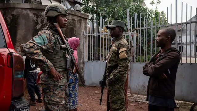 Deux militaires armés accompagnés d'un civil en arrière-plan, dans une zone de conflit